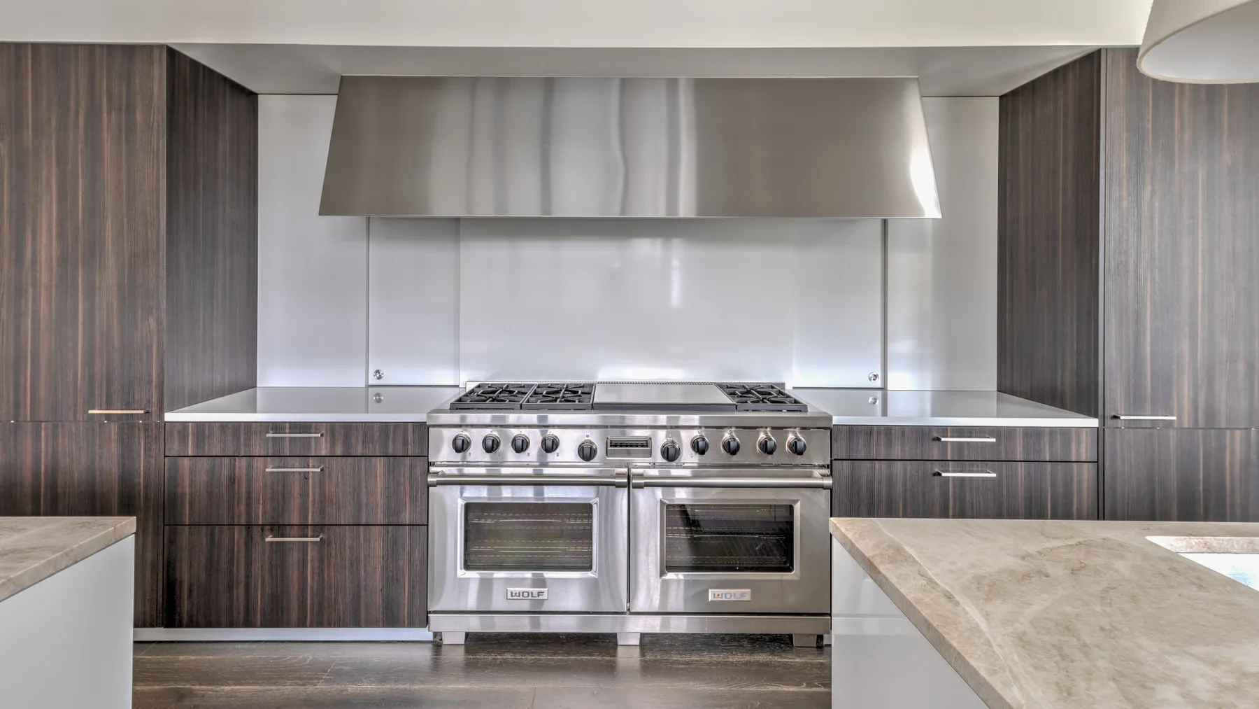 A modern kitchen with stainless steel ovens beneath a broad range hood.