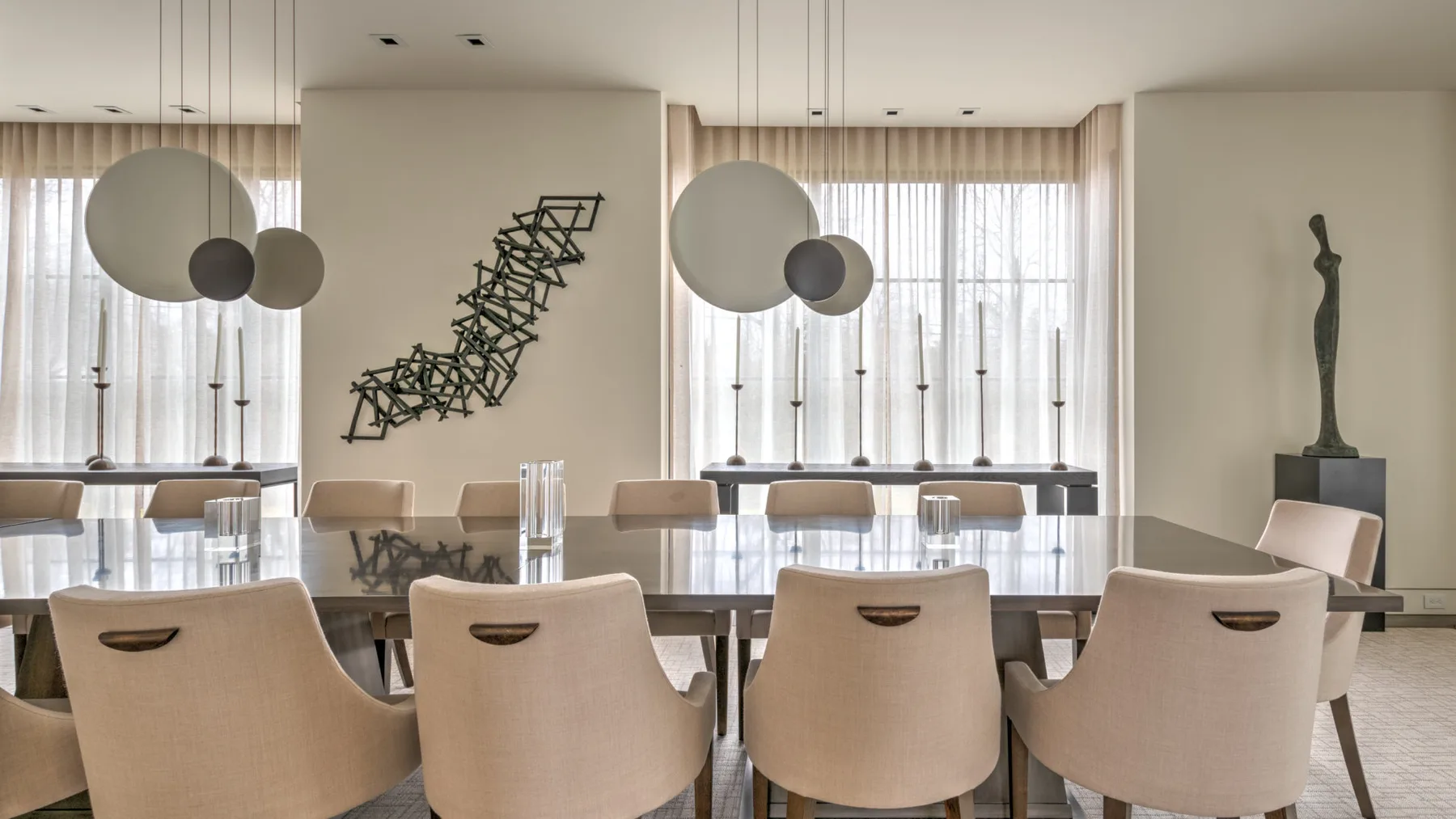 A dining area with a long table, upholstered seating, and pendant lights.