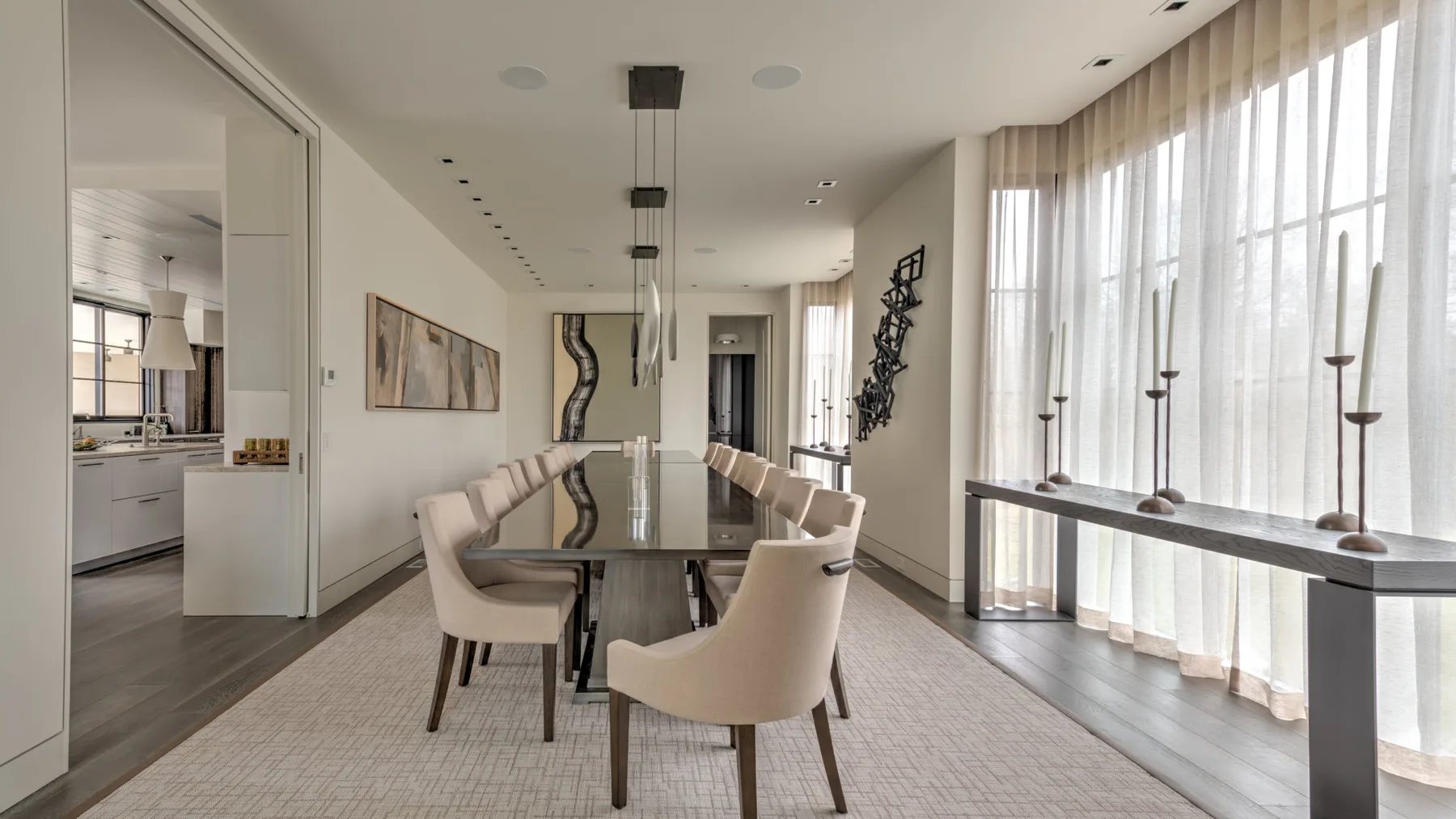 A modern dining area with a long table beside floor-to-ceiling windows.