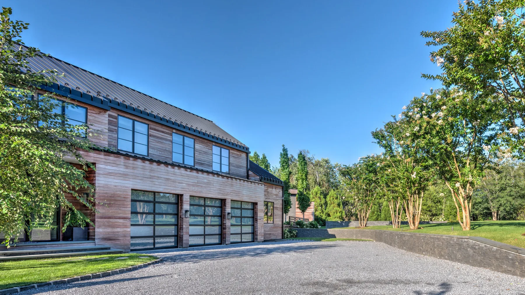 A modern building faces a paved driveway, with trees and greenery around it.