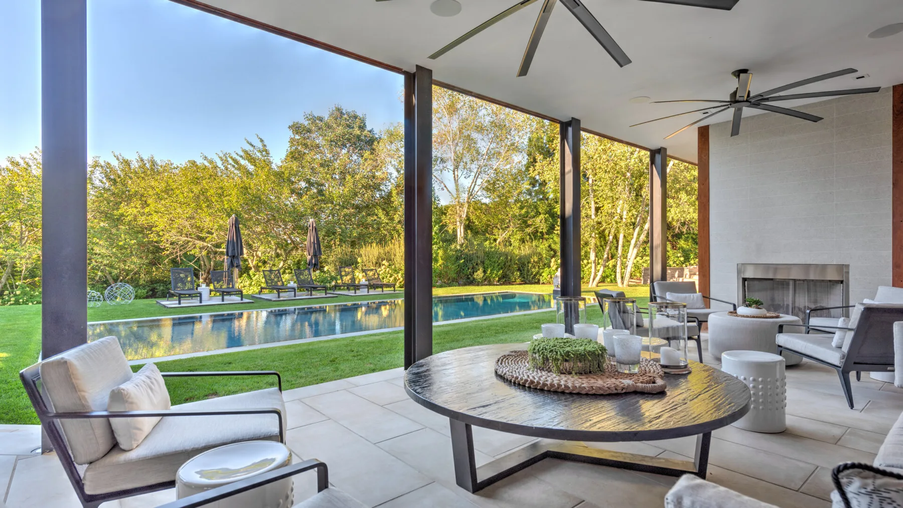 A covered patio overlooks a swimming pool, with outdoor seating and a round table.