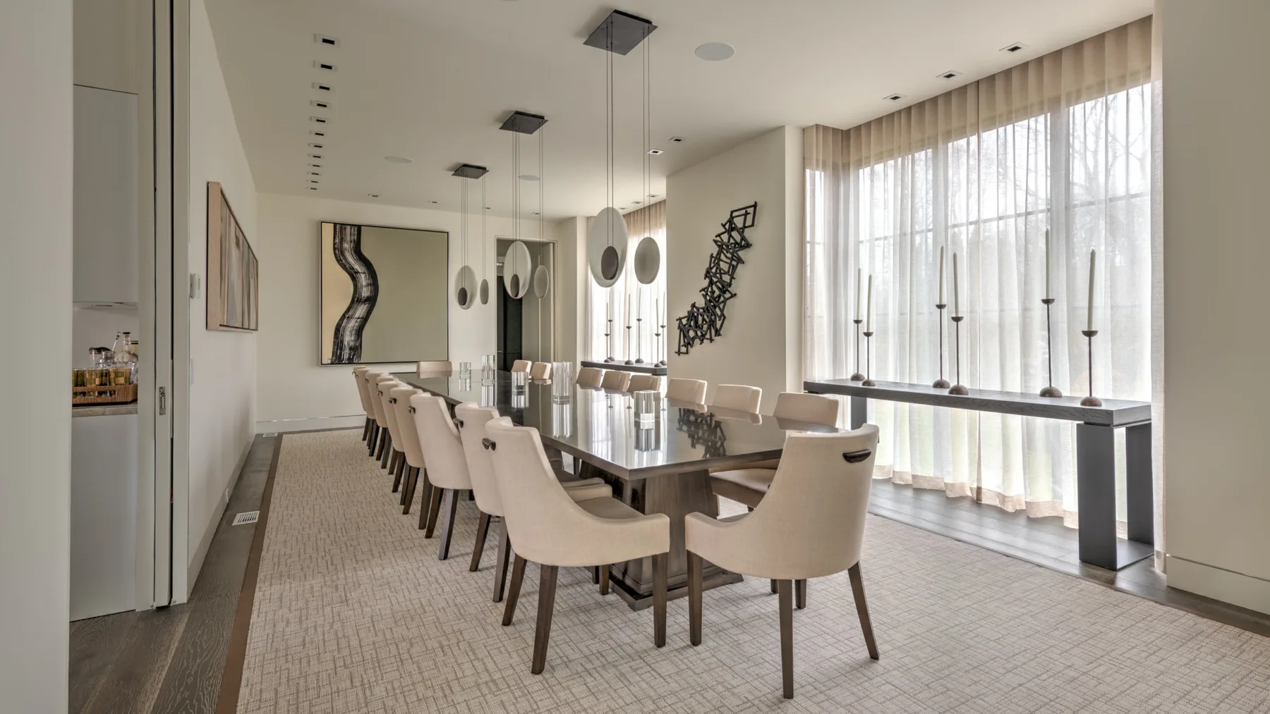 A bright dining room with a long table and large curtained windows.