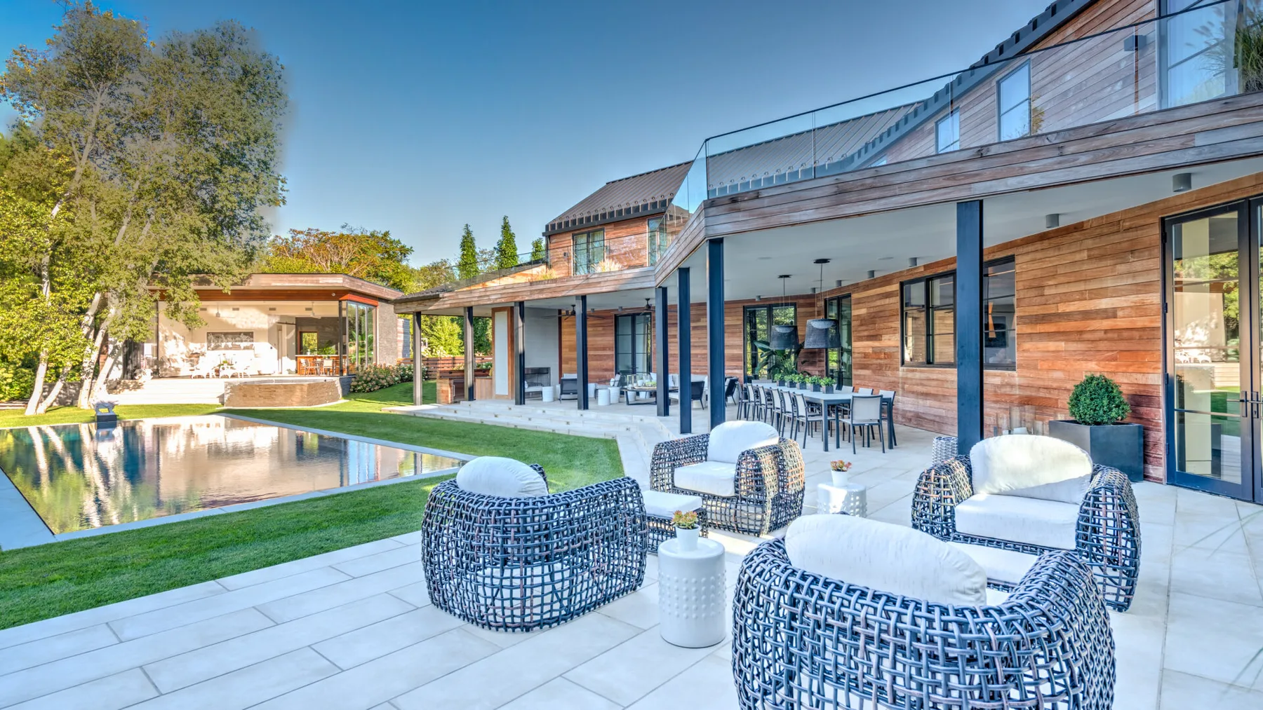 A modern house opens onto a paved patio with outdoor seating and a pool.