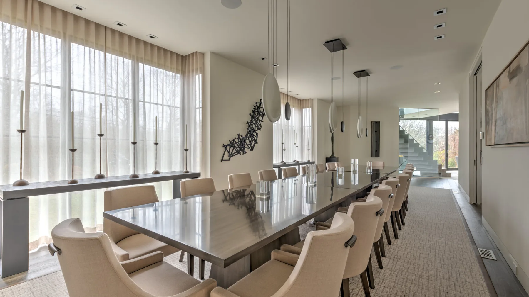 A bright dining room with a long table and upholstered seating beside tall windows.