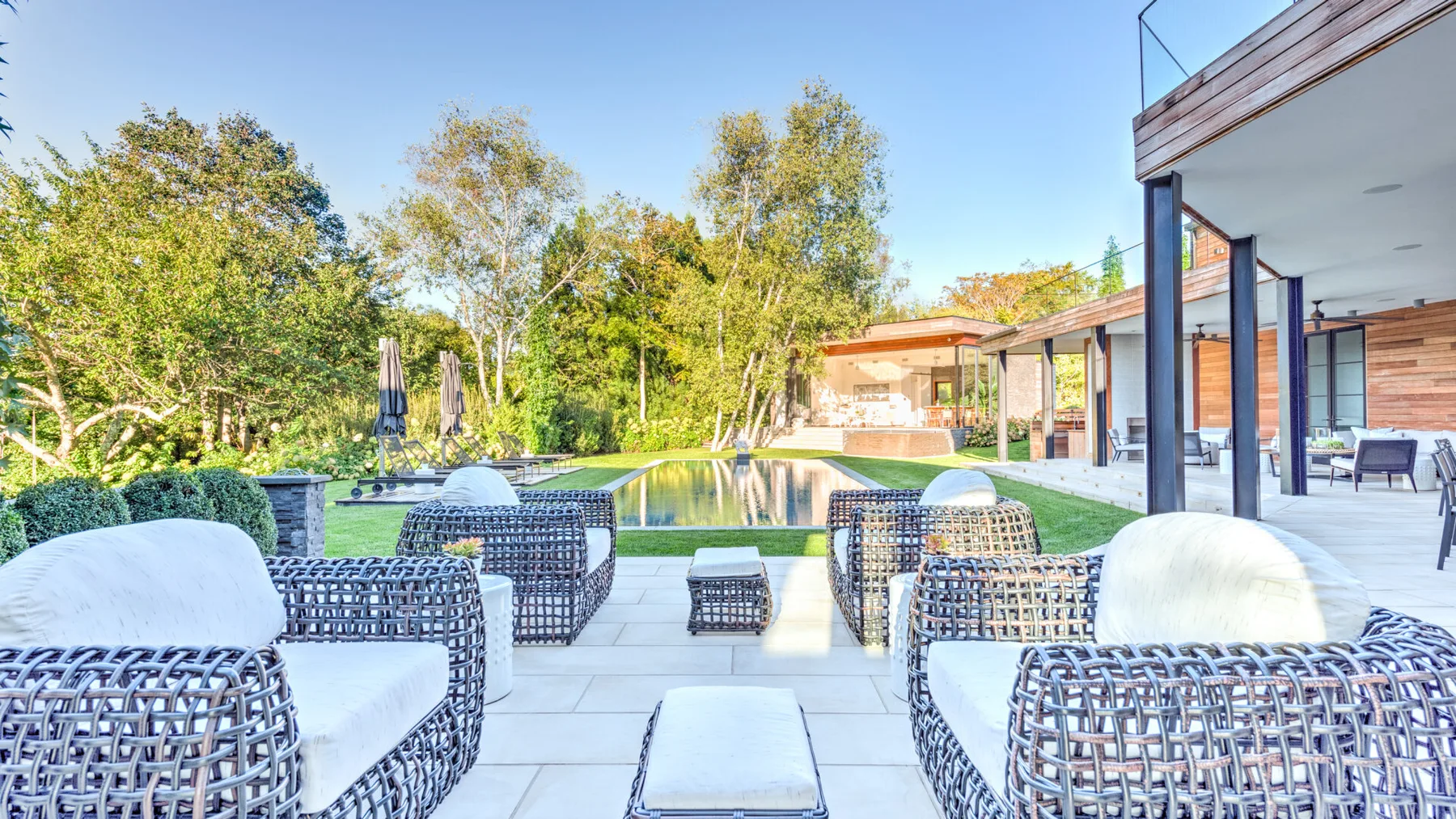 An outdoor patio with woven seating beside a swimming pool and trees.