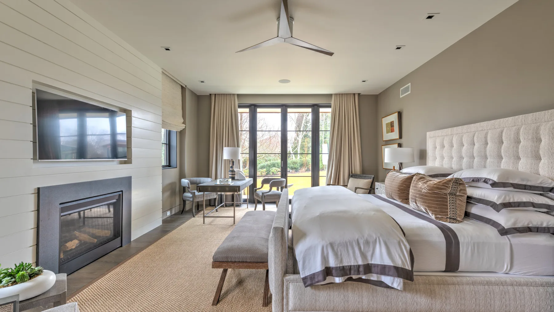 A bright bedroom with a large bed, a bench, and sliding glass doors.