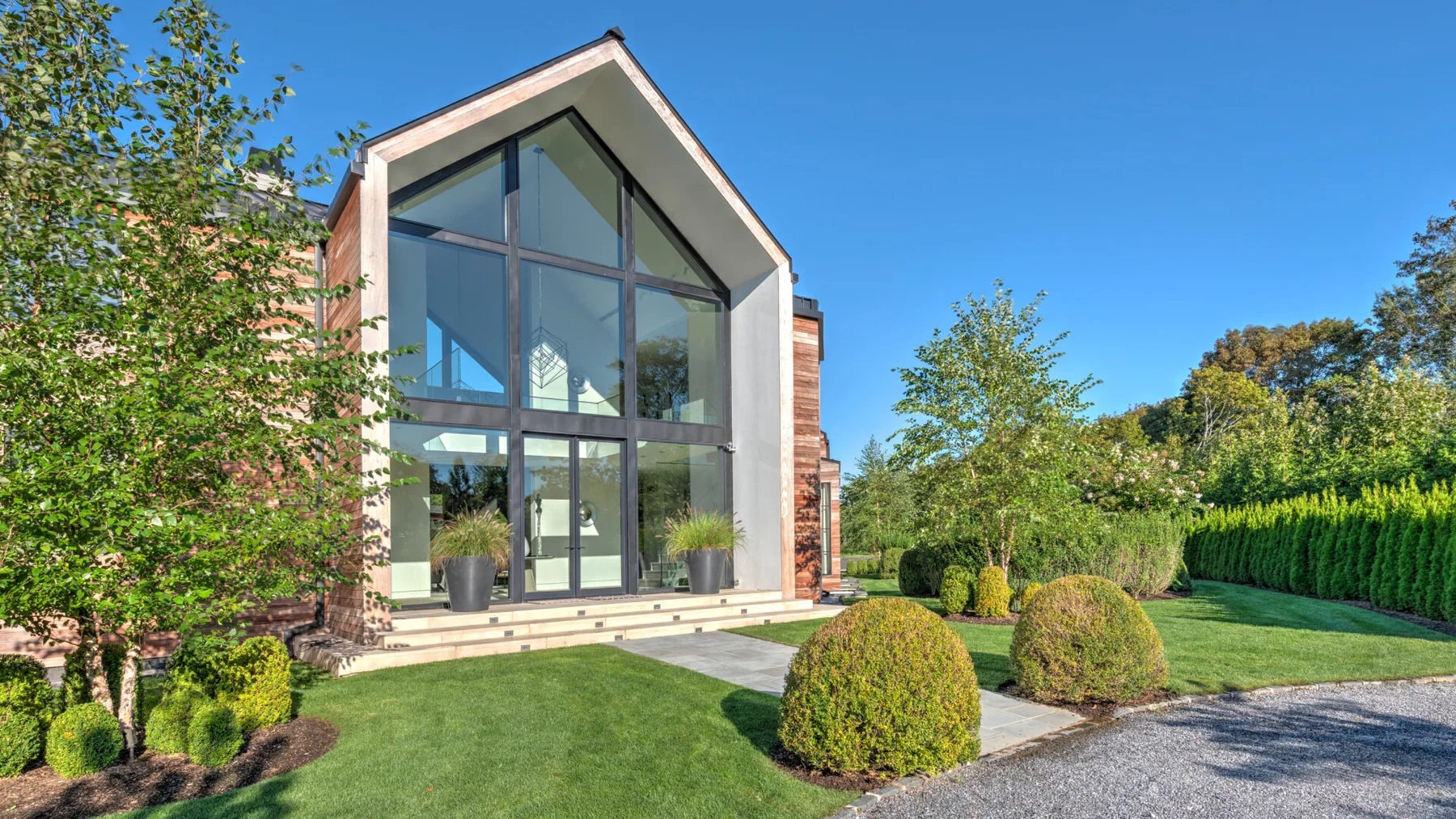 A modern house with a tall glass facade overlooks a landscaped lawn.