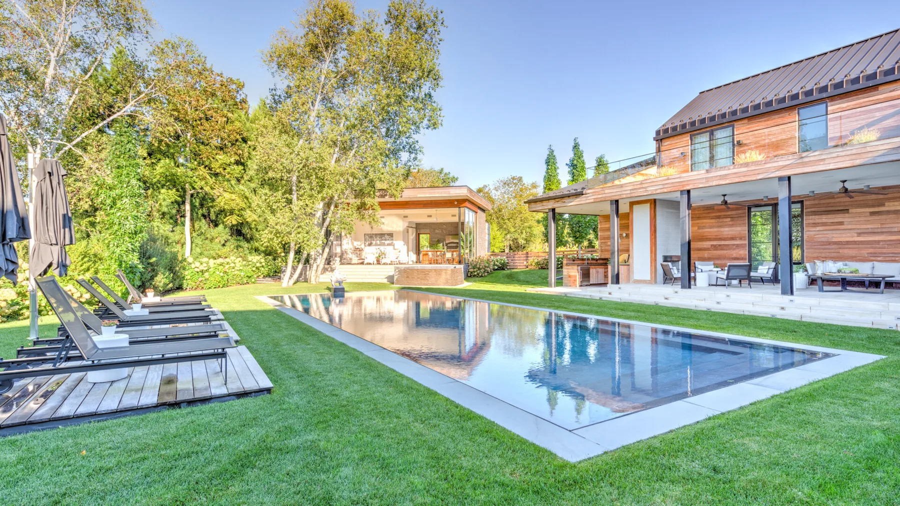 A landscaped outdoor pool beside a modern house and wooden lounge seating.