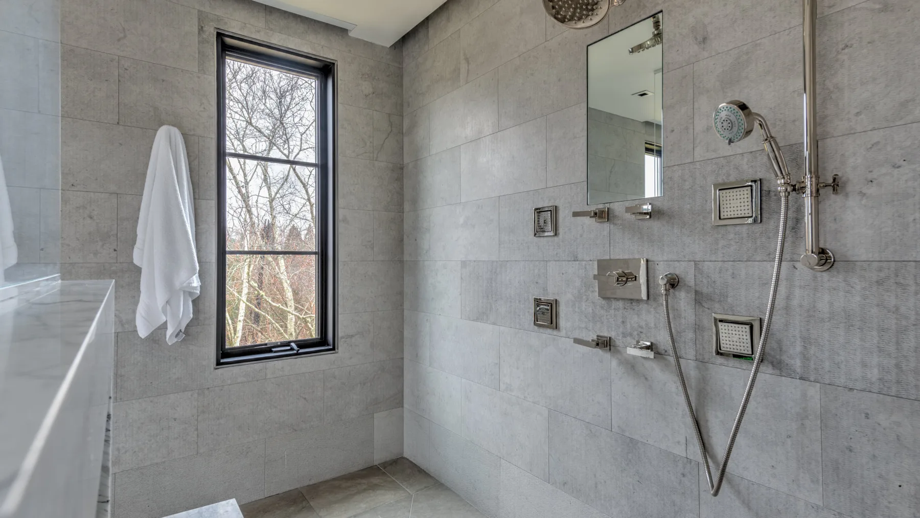 A tiled bathroom with a wall-mounted shower and a window.