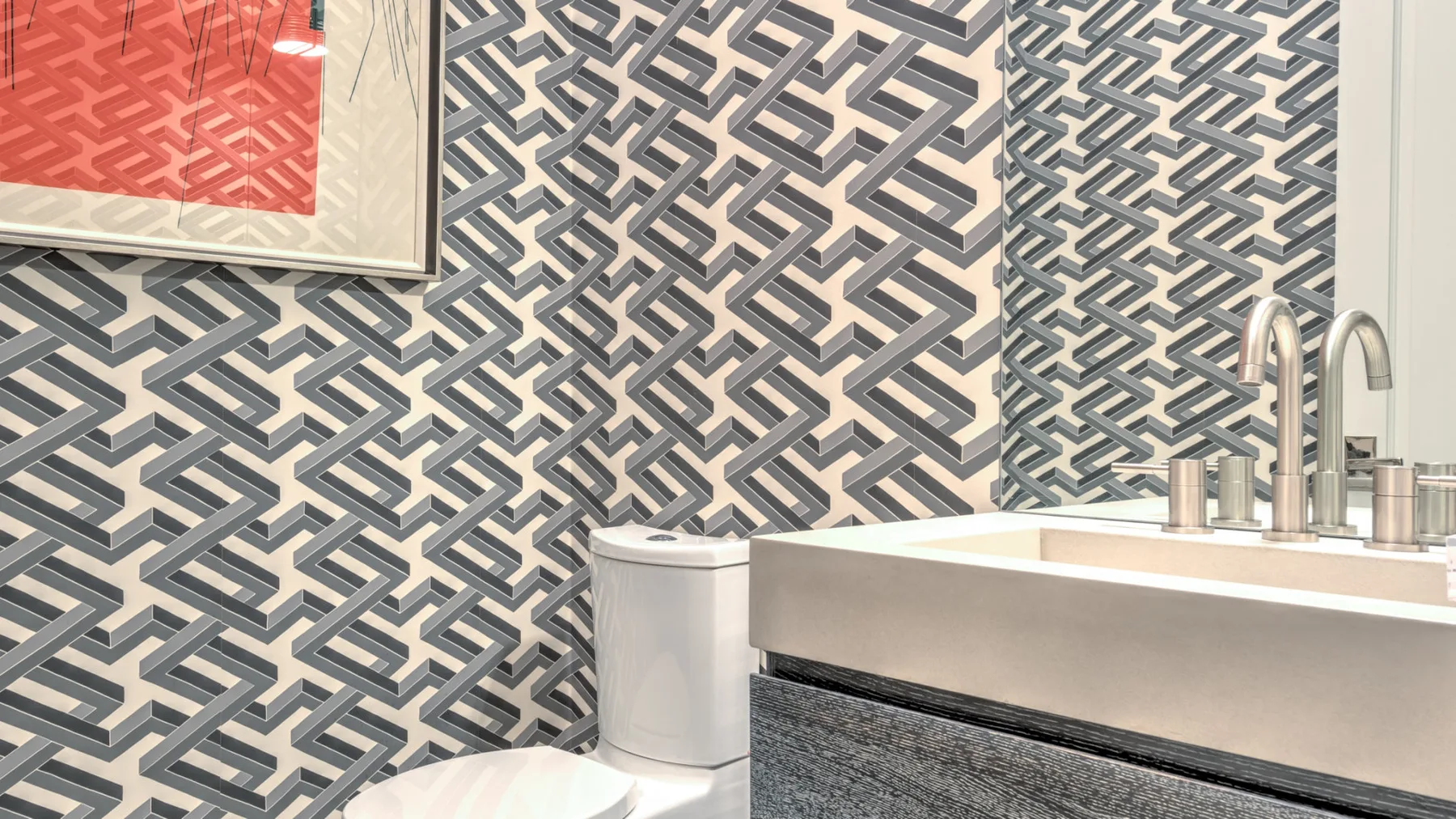 A bathroom vanity and toilet sit against a wall with geometric patterned wallpaper.