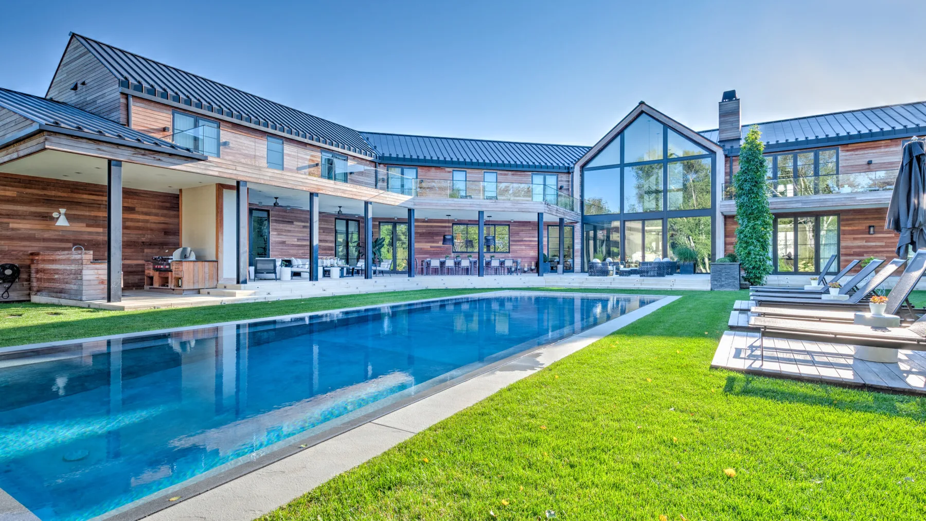 A modern house surrounds a long swimming pool and a grassy lawn.
