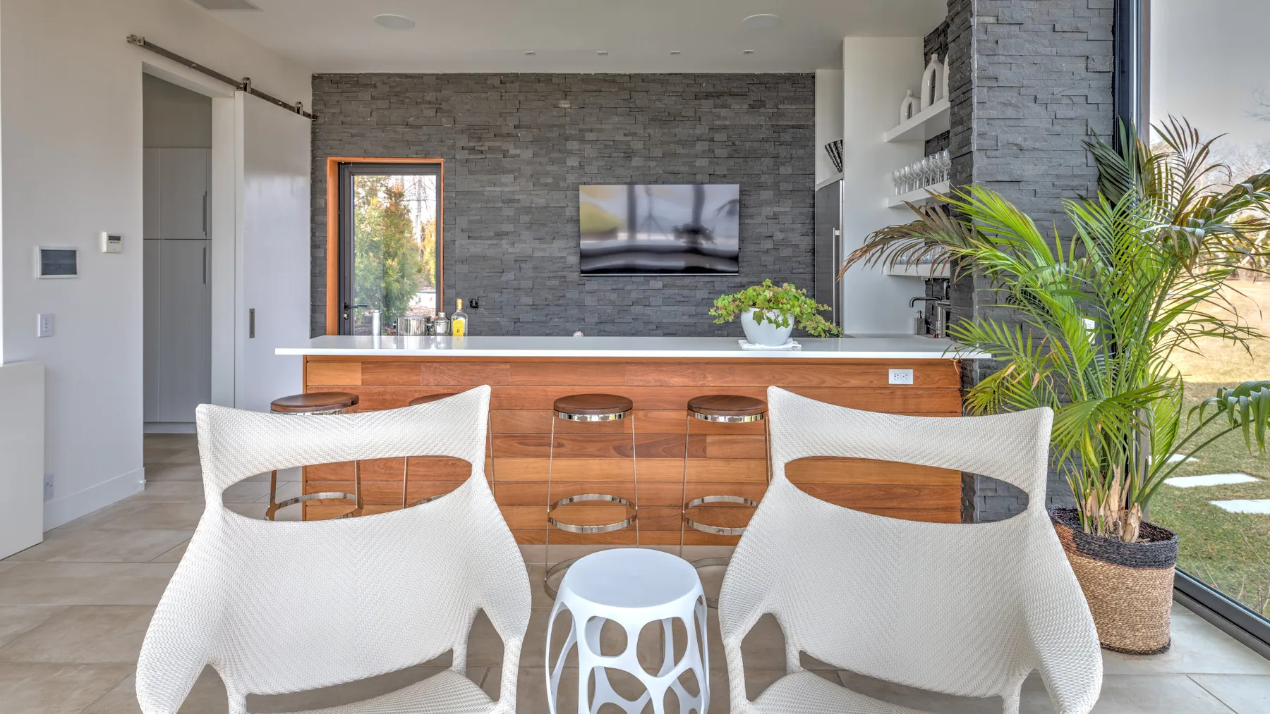 A modern bar area with white seating, a stone accent wall, and a large window.