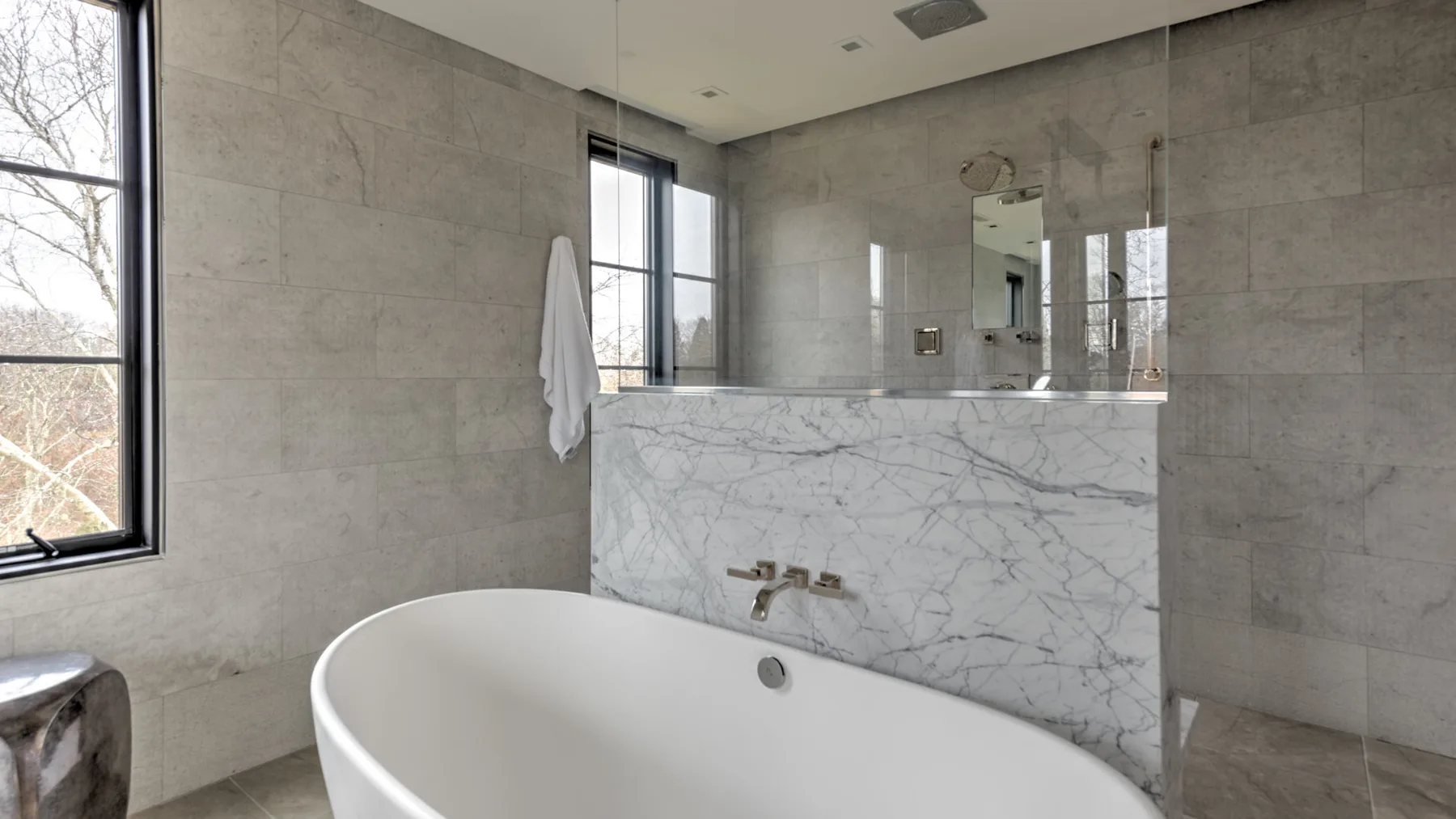 A bright bathroom with a freestanding bathtub and a marble-look wall.