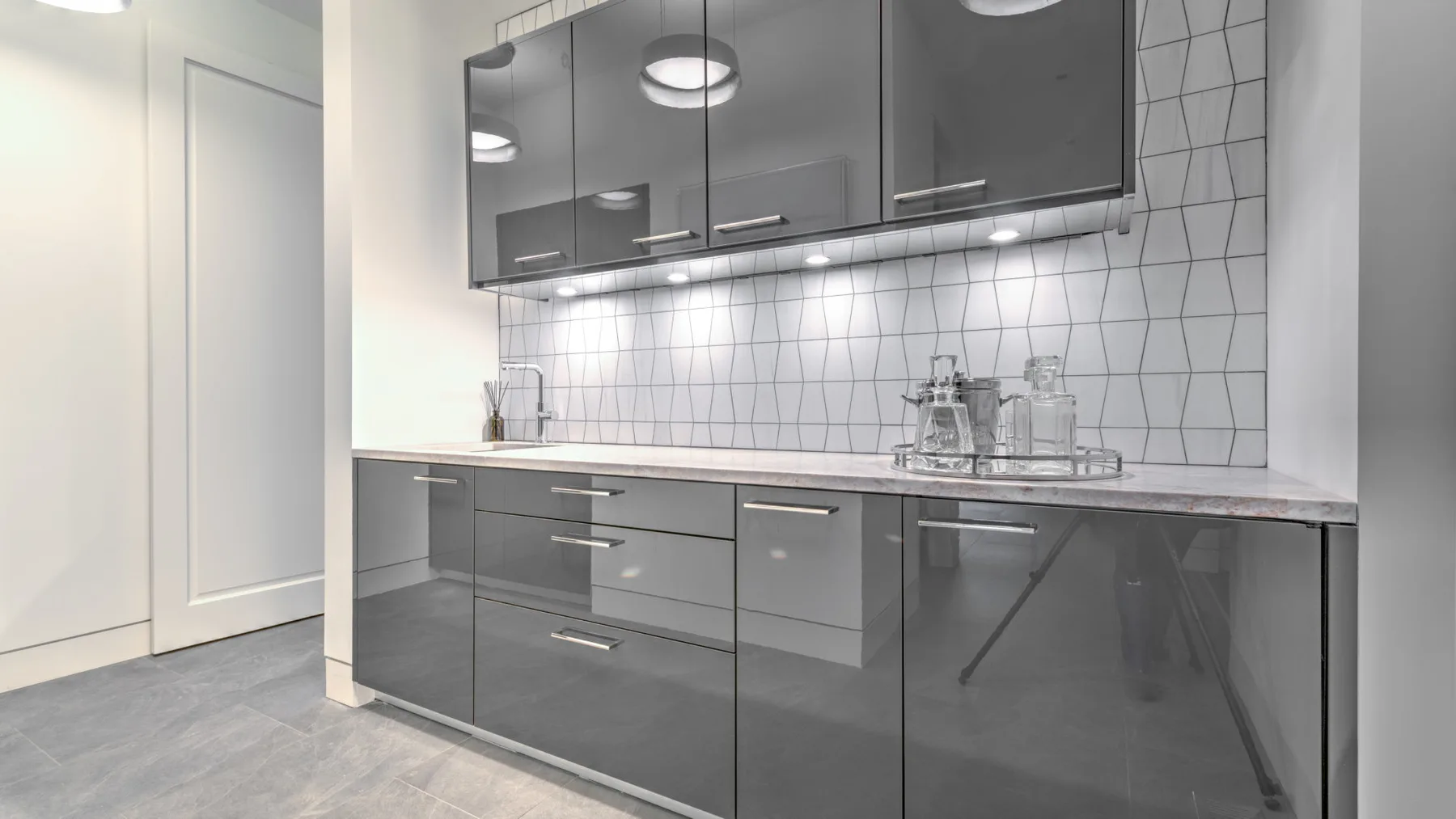 A modern kitchen with dark cabinets, a light countertop, and a tiled backsplash.