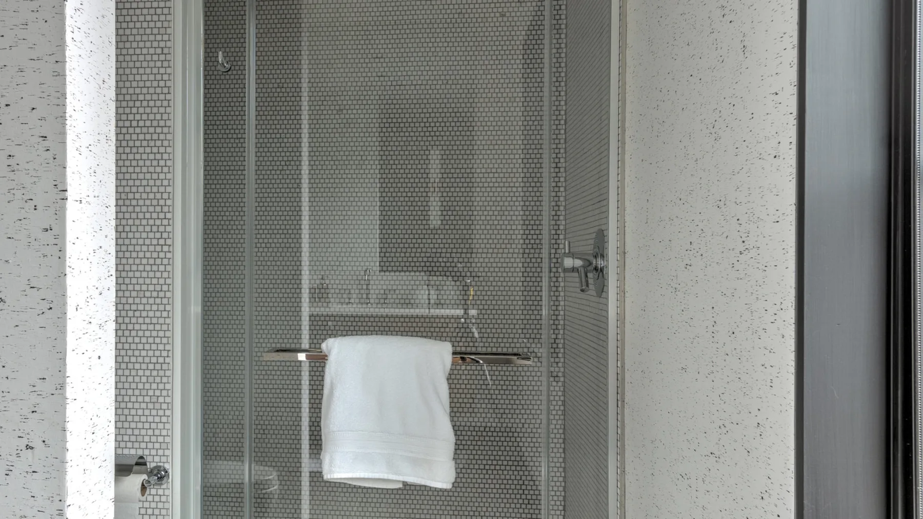 A tiled shower area with a white towel hanging over the glass panel.