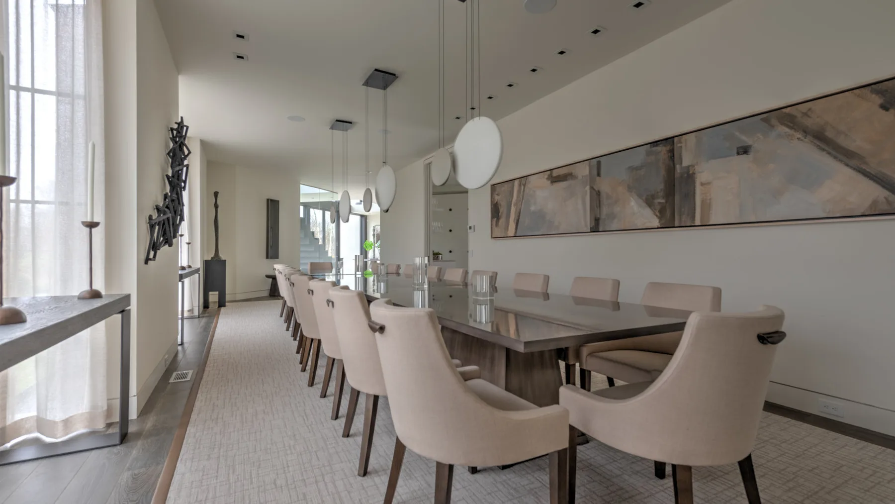 A dining area with a long table, upholstered seating, and pendant lights.