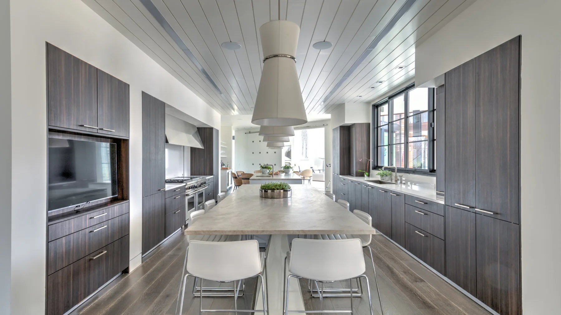 A long kitchen with a central island, dark cabinetry, and large windows.