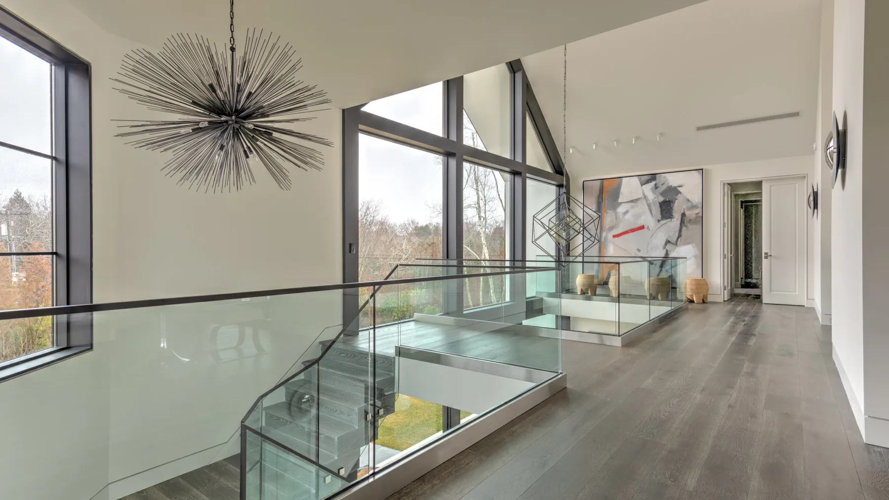 A bright modern interior with a glass-railed staircase and large windows.