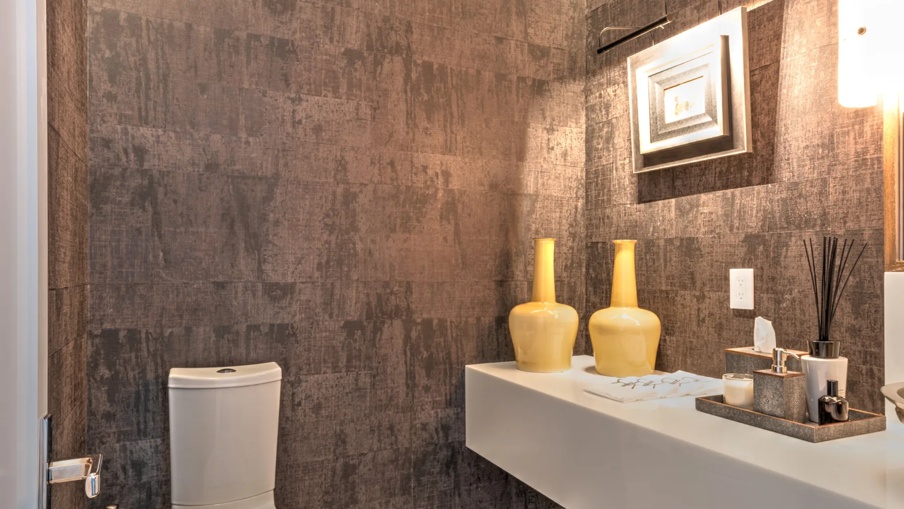 A bathroom vanity with yellow vases and a toilet against a dark textured wall.
