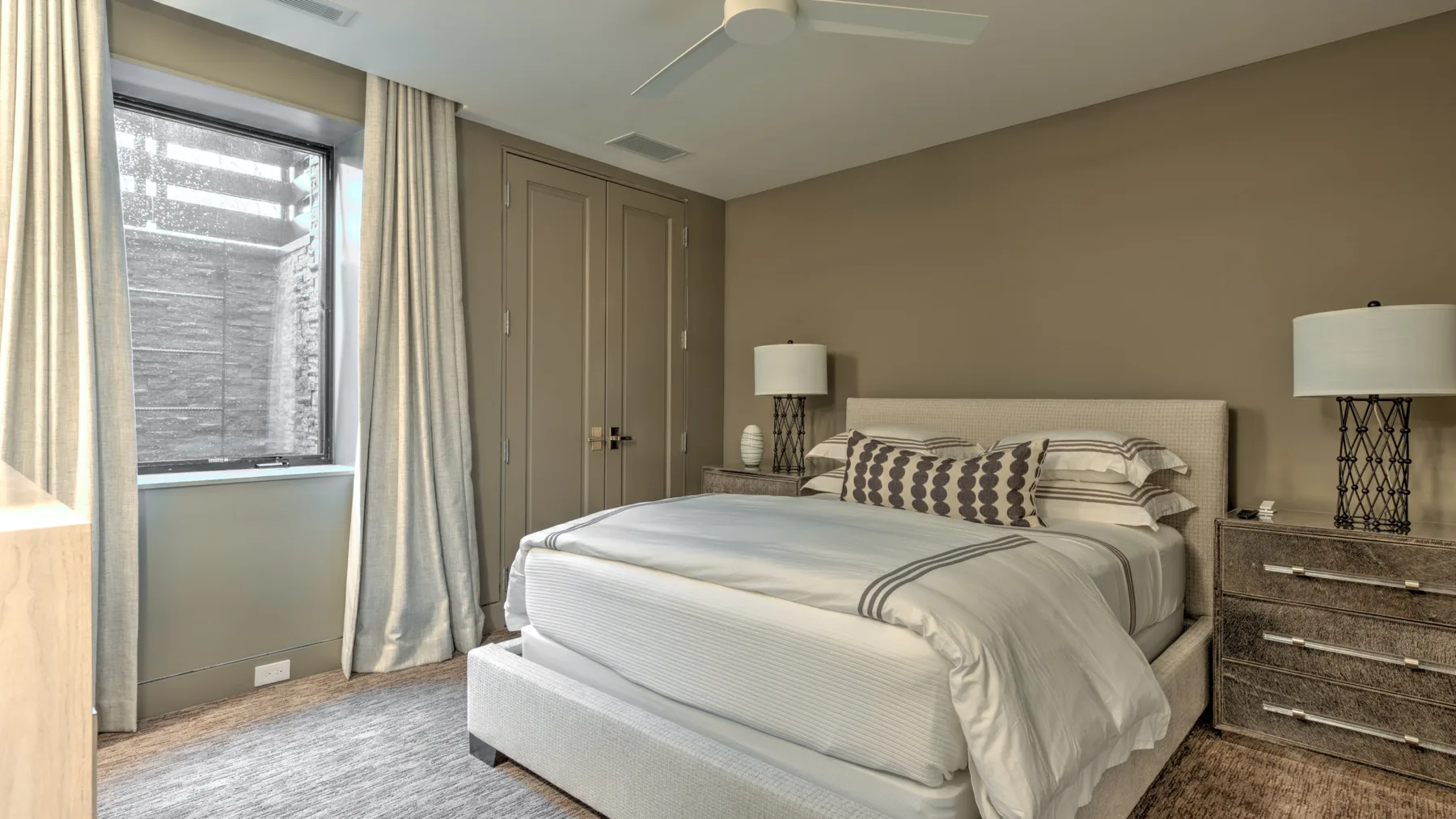 A bedroom with a neatly made bed beside a curtained window.