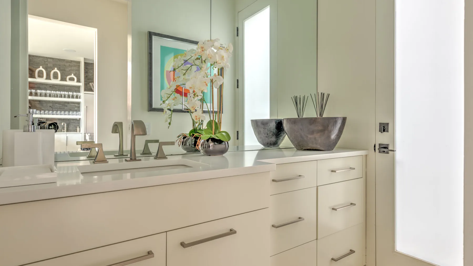 A bright bathroom vanity with a mirror, sink, and orchid arrangement.