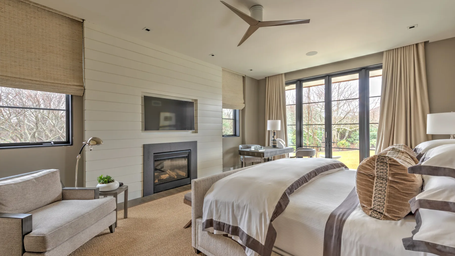 A bedroom with a large bed, seating, and windows overlooking a garden.
