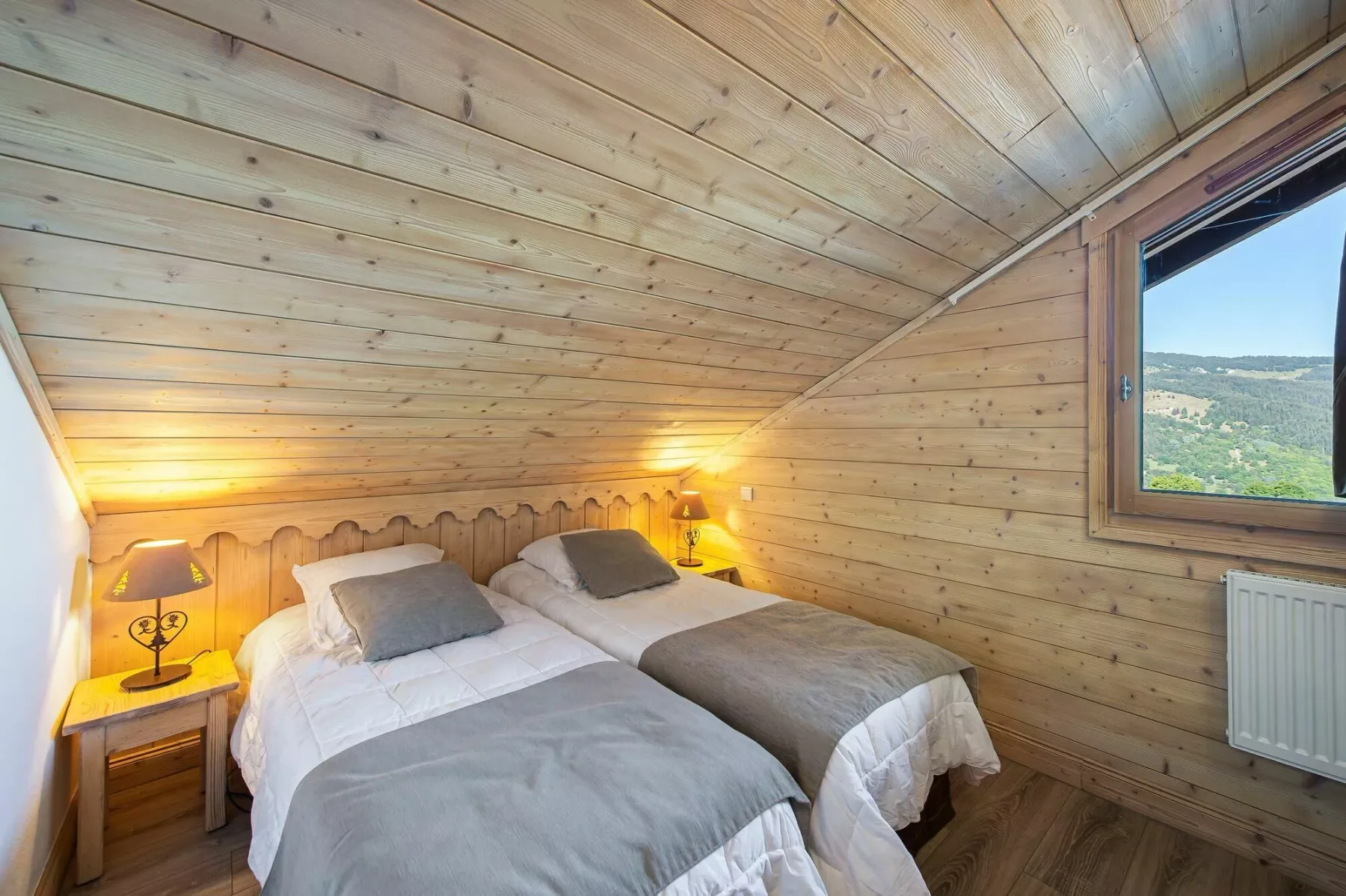 A wood-paneled bedroom with two beds and a window overlooking hills.