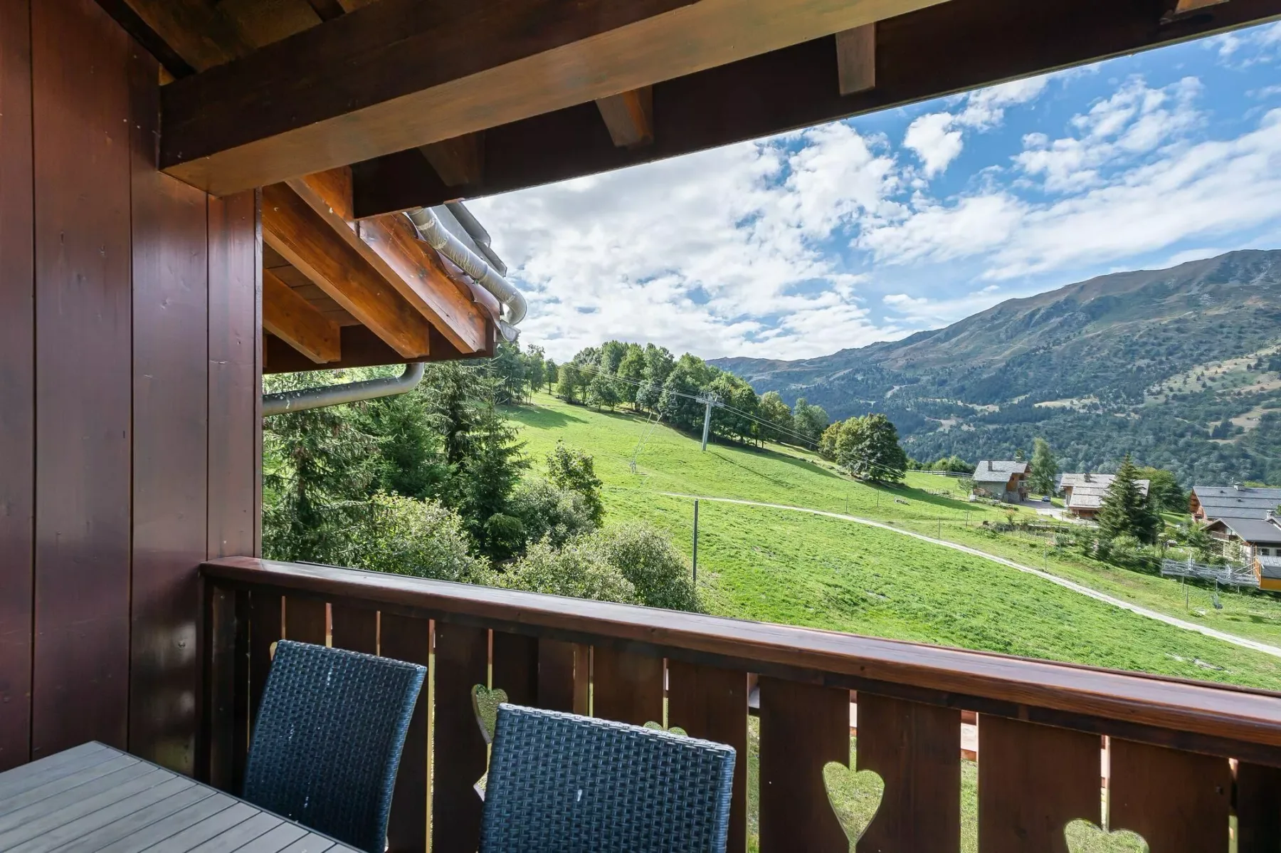 A covered balcony overlooks a green hillside and mountain valley.