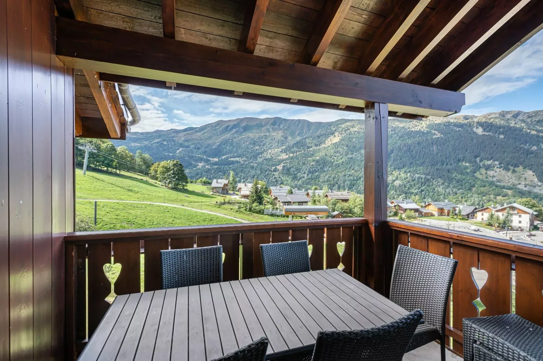 A covered balcony dining area overlooks a green mountain valley.