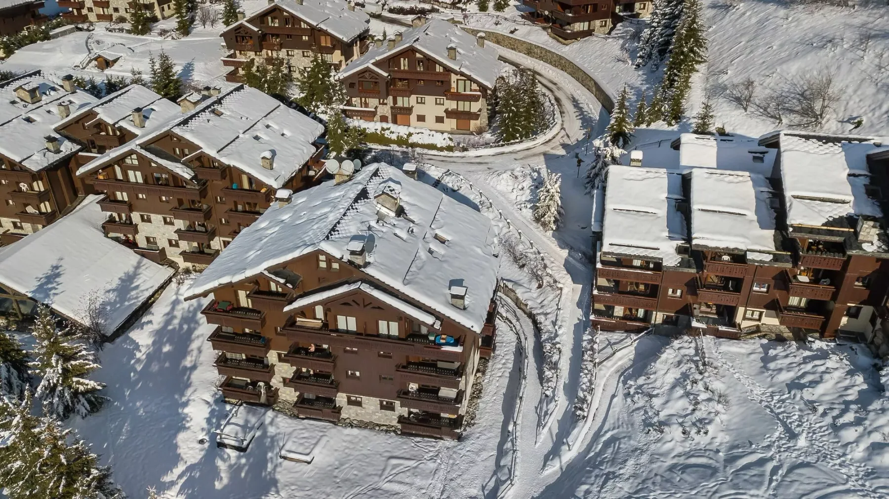Aerial view of snow-covered chalet-style buildings along a winding road.