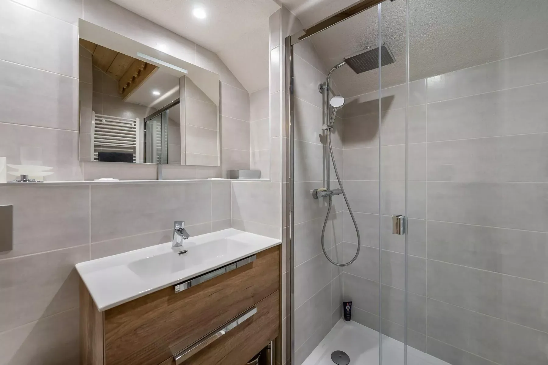 A tiled bathroom with a wood-front vanity and a glass shower.