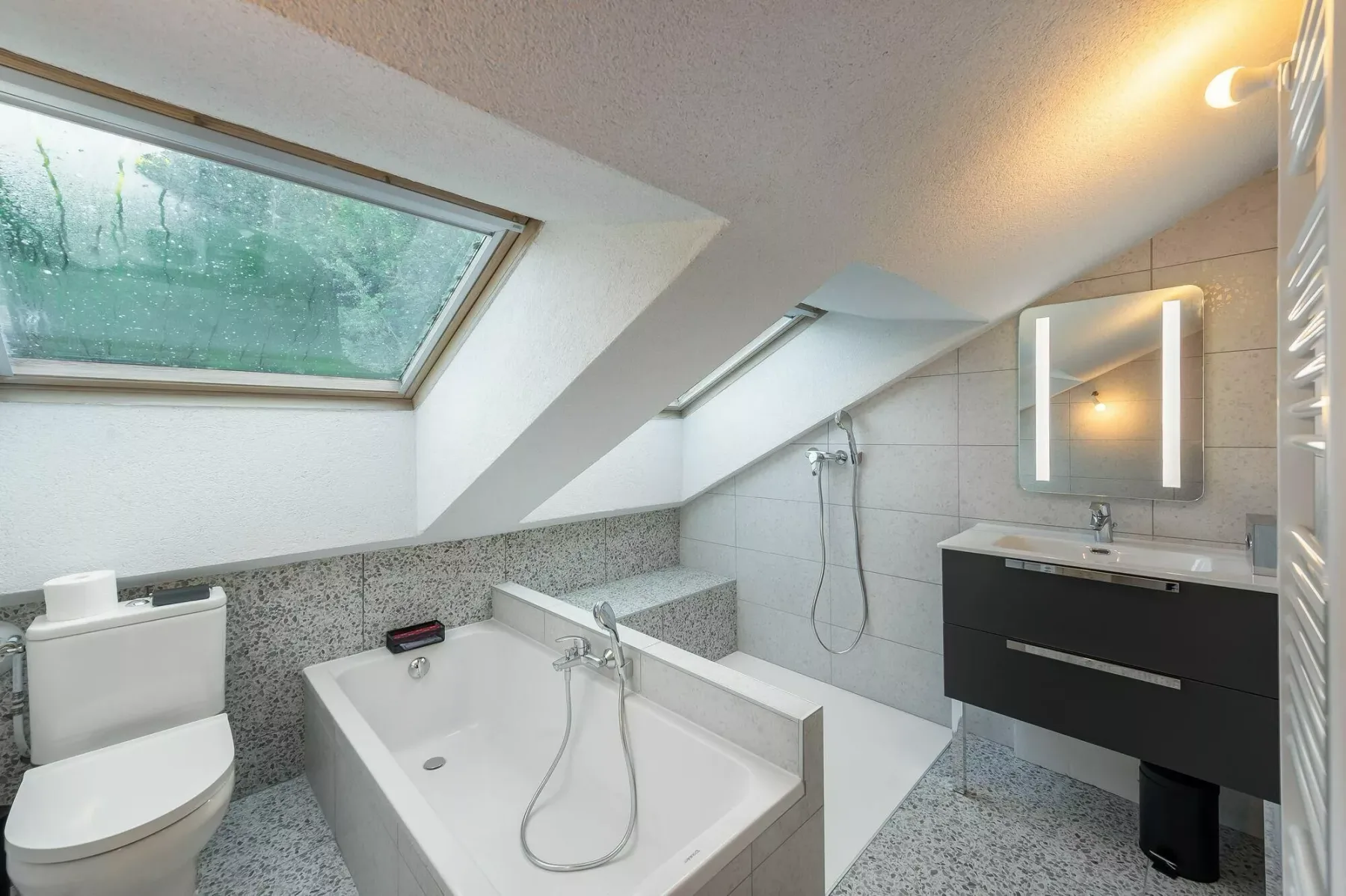 A bathroom with a bathtub, toilet, and vanity beneath a sloped ceiling.