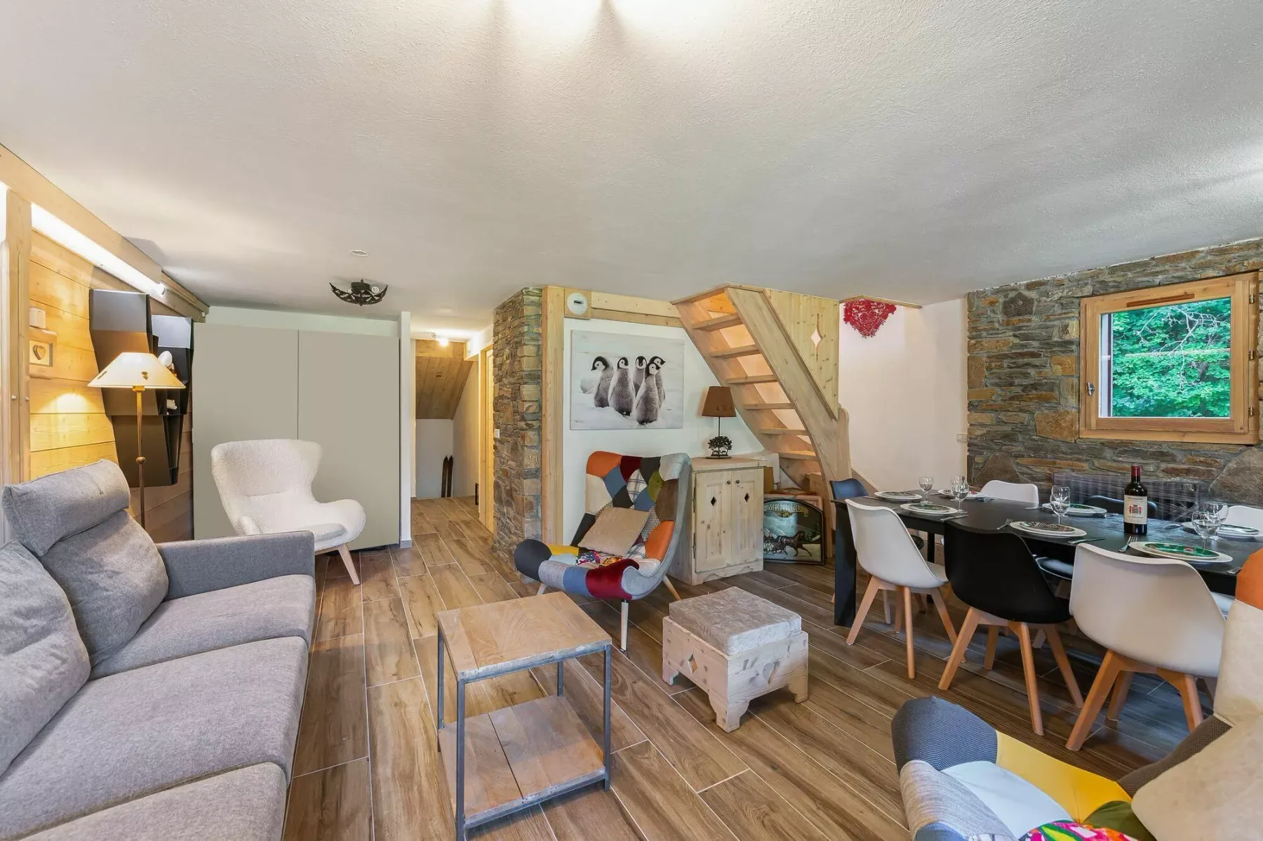 A rustic living and dining room with seating, a wooden staircase, and a set table.