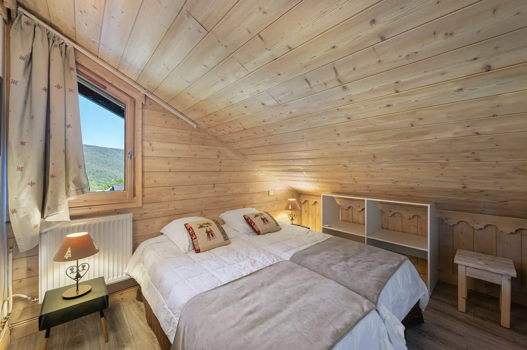 A bedroom with a bed, bedside lamp, and window overlooking a green hillside.
