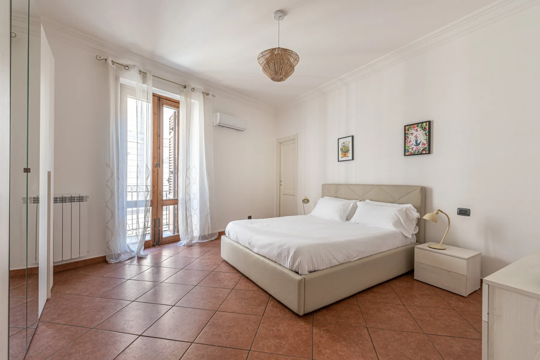 Un dormitorio luminoso con una cama grande, una mesita de noche y puertas altas de vidrio.