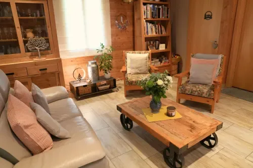Salón revestido de madera en Gîte La Péniche, con un sofá de cuero, sillones, chimenea y estanterías para libros.