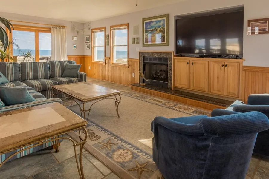 A living room with seating, coffee tables, and a fireplace beneath a wall-mounted television.