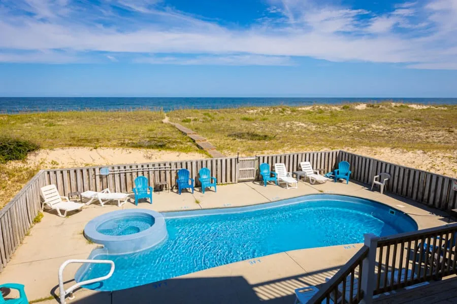 Una piscina al aire libre y un spa están junto a una playa de arena, con asientos alrededor de la terraza.