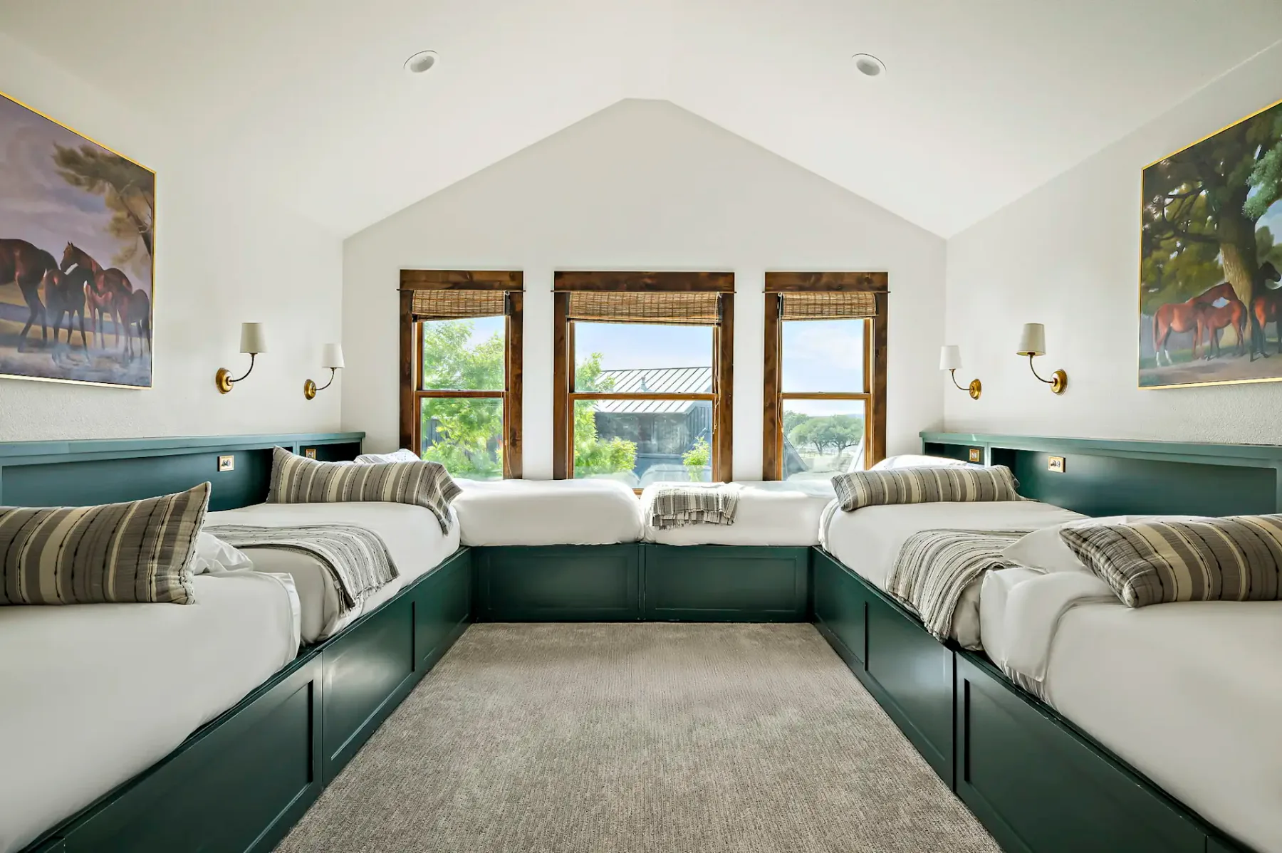 Un dormitorio luminoso con varias camas, estructuras verdes y ventanas con vistas a la vegetación.