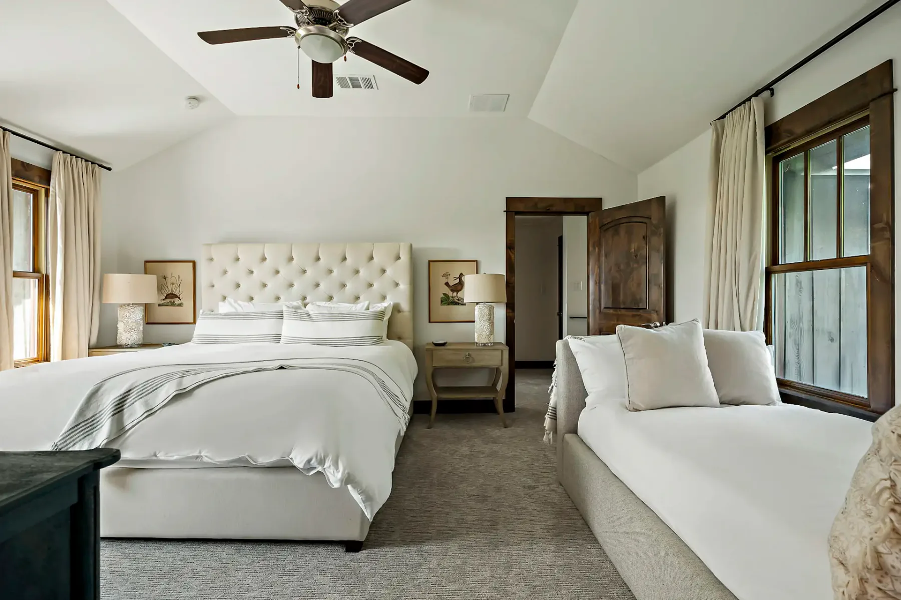Dormitorio elegante con una cama grande, una acogedora chaise longue, ventilador de techo e iluminación suave. Los tonos neutros y los detalles de madera crean un ambiente sereno.