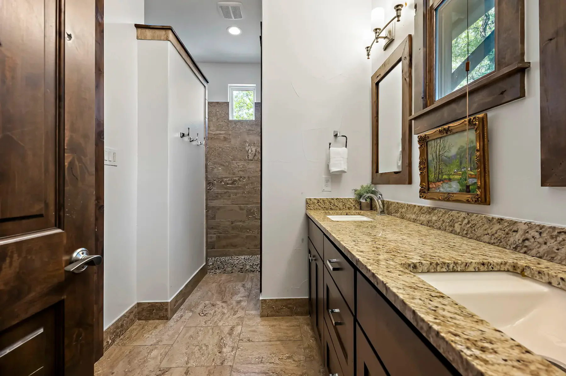 Un baño con un lavabo largo, cuadros enmarcados y una ducha al fondo.