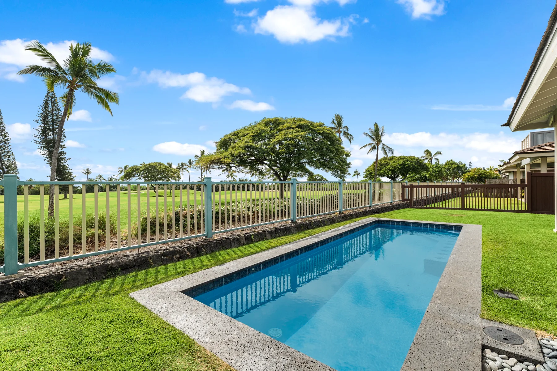 Una piscina al aire libre está junto a un jardín con césped y un paisaje abierto cercado.