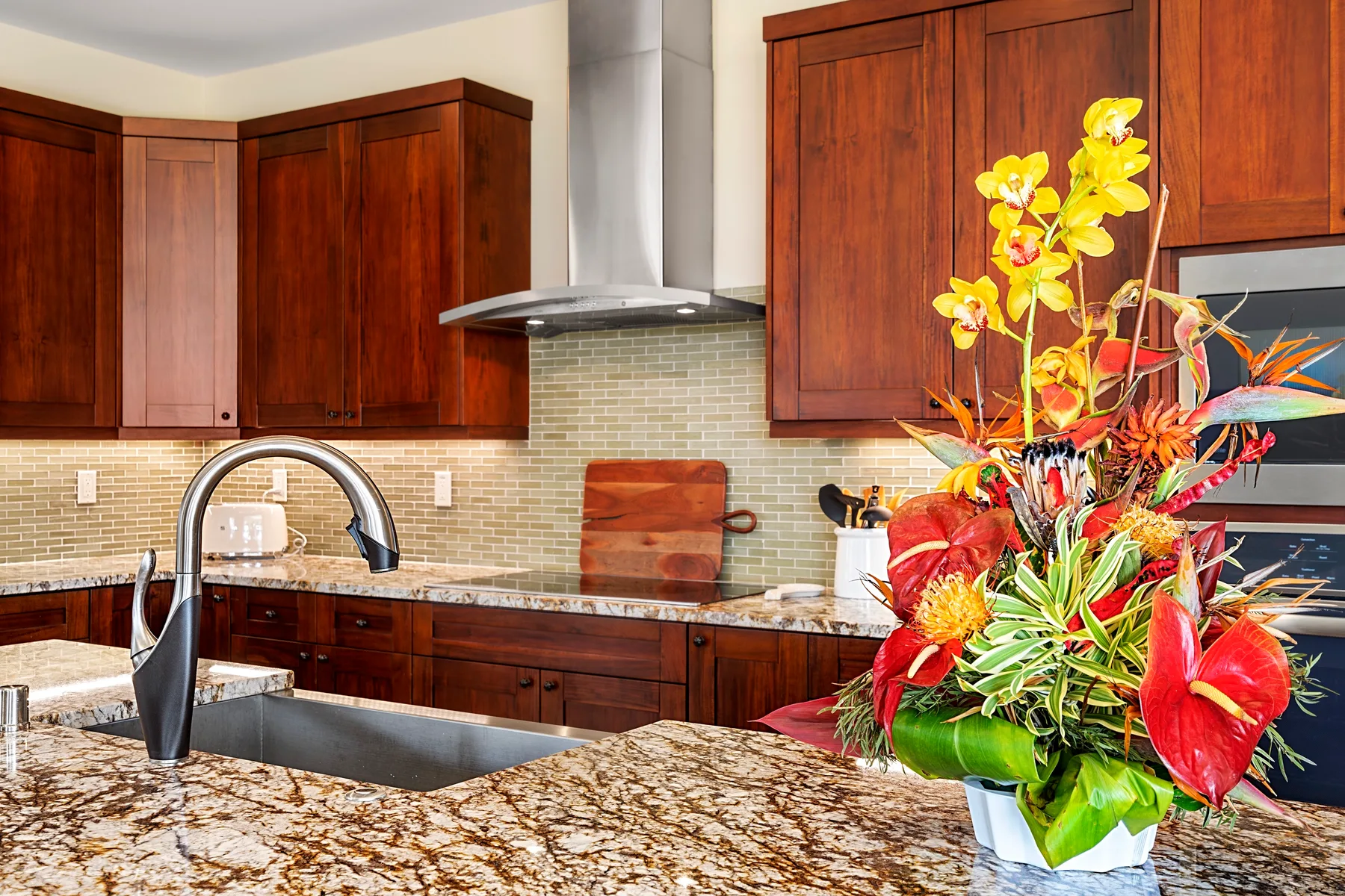 Una cocina con gabinetes de madera oscura, una encimera moteada y un arreglo floral colorido.