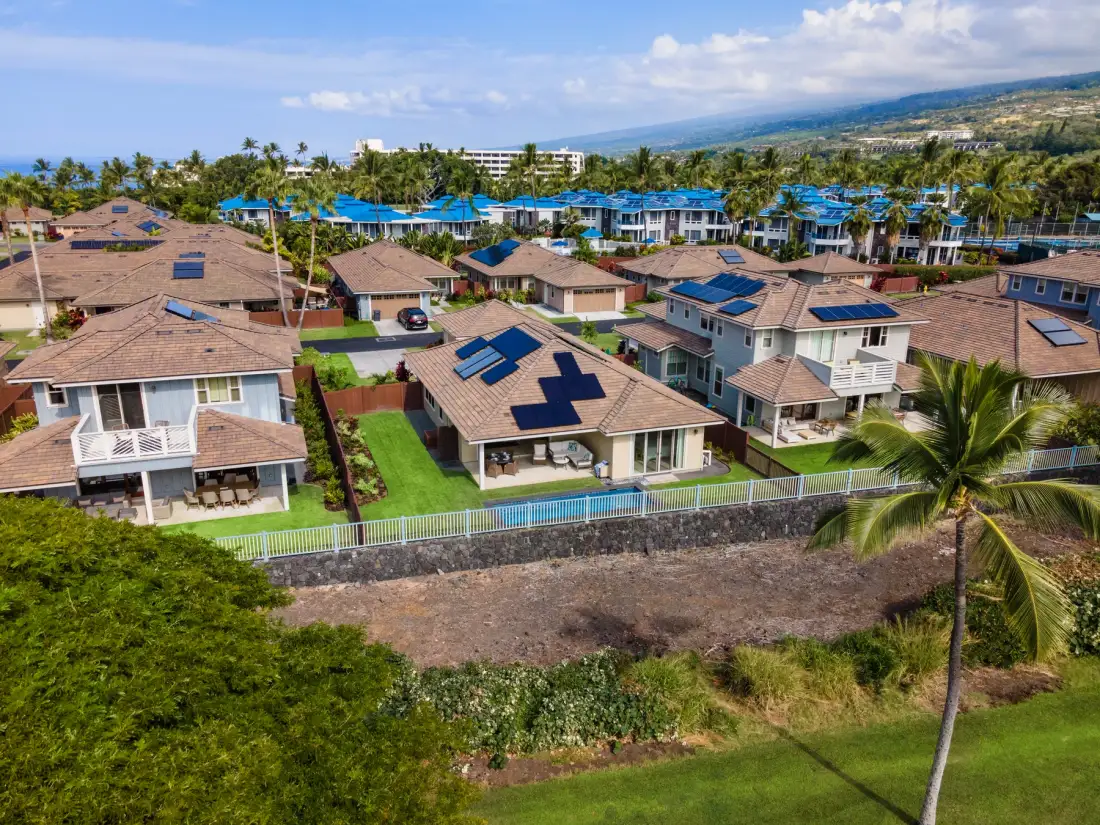 Vista aérea de un barrio residencial con casas y palmeras.