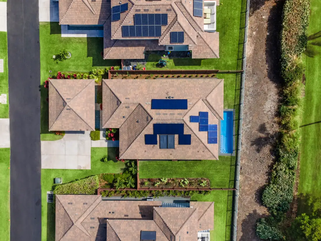 Una vista aérea muestra varias casas con paneles solares, jardines y una carretera.