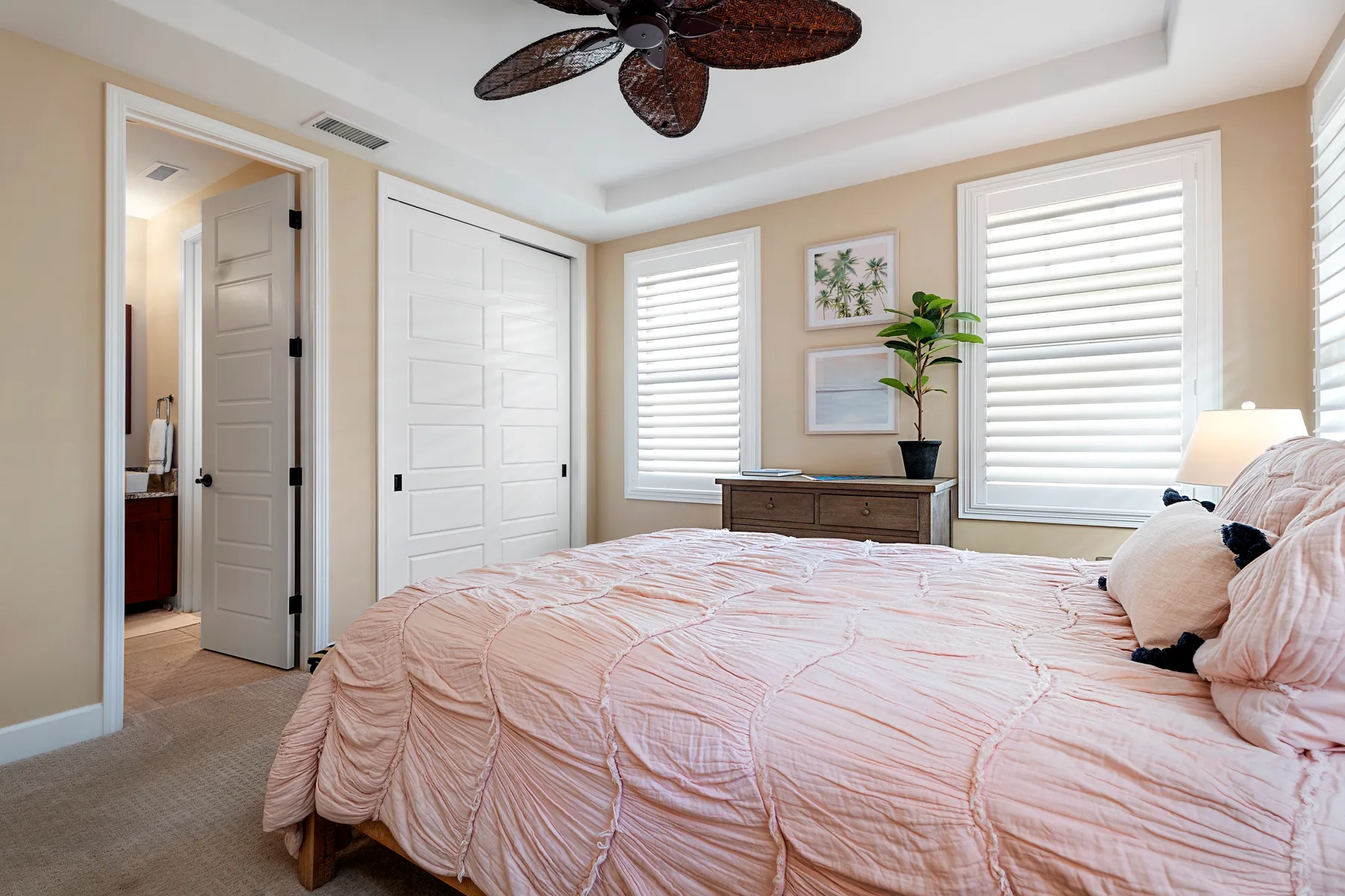 Un dormitorio con una cama, contraventanas blancas y un ventilador de techo.