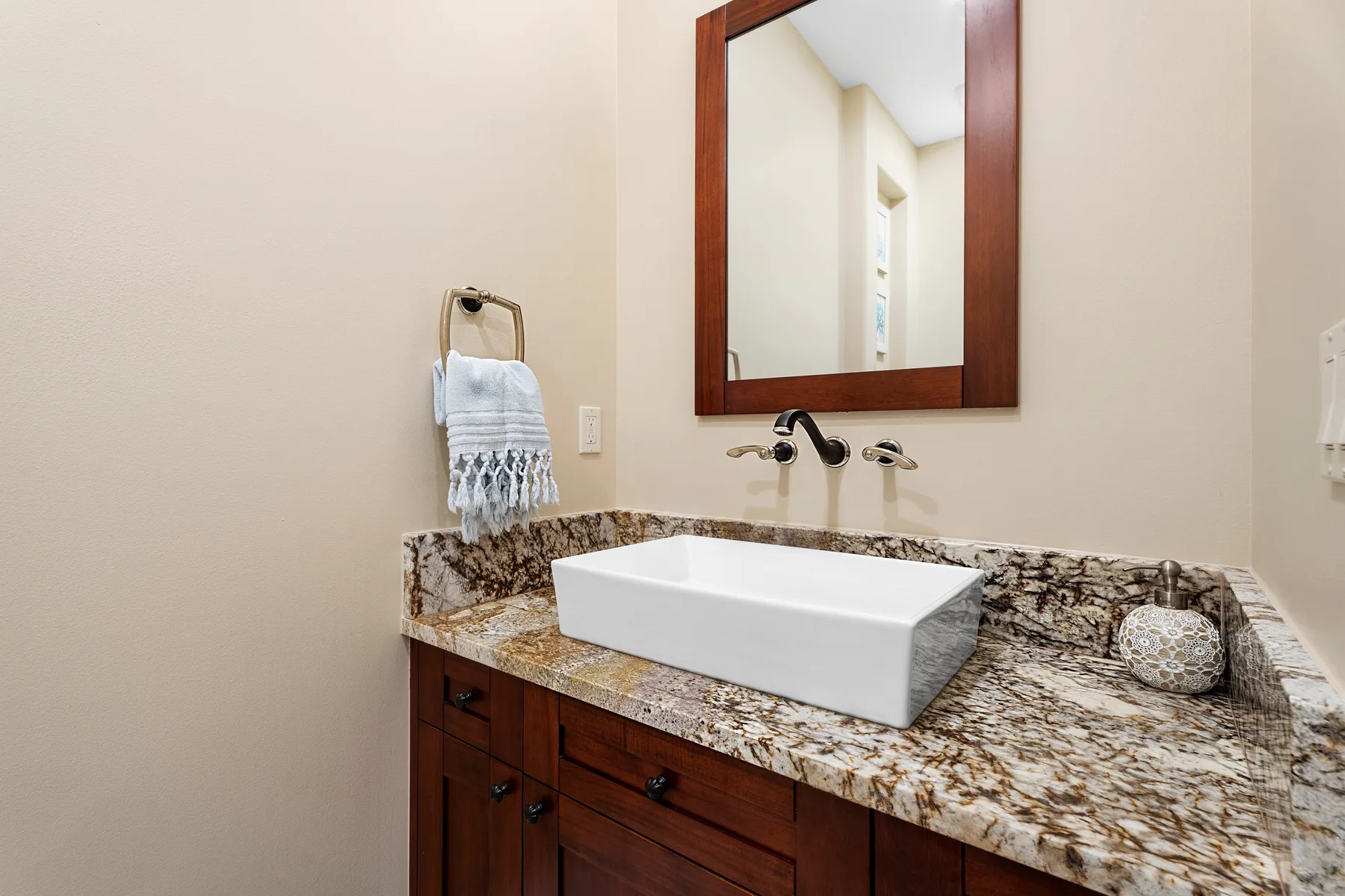 Un tocador de baño con lavabo blanco sobre encimera, espejo y grifo de pared.