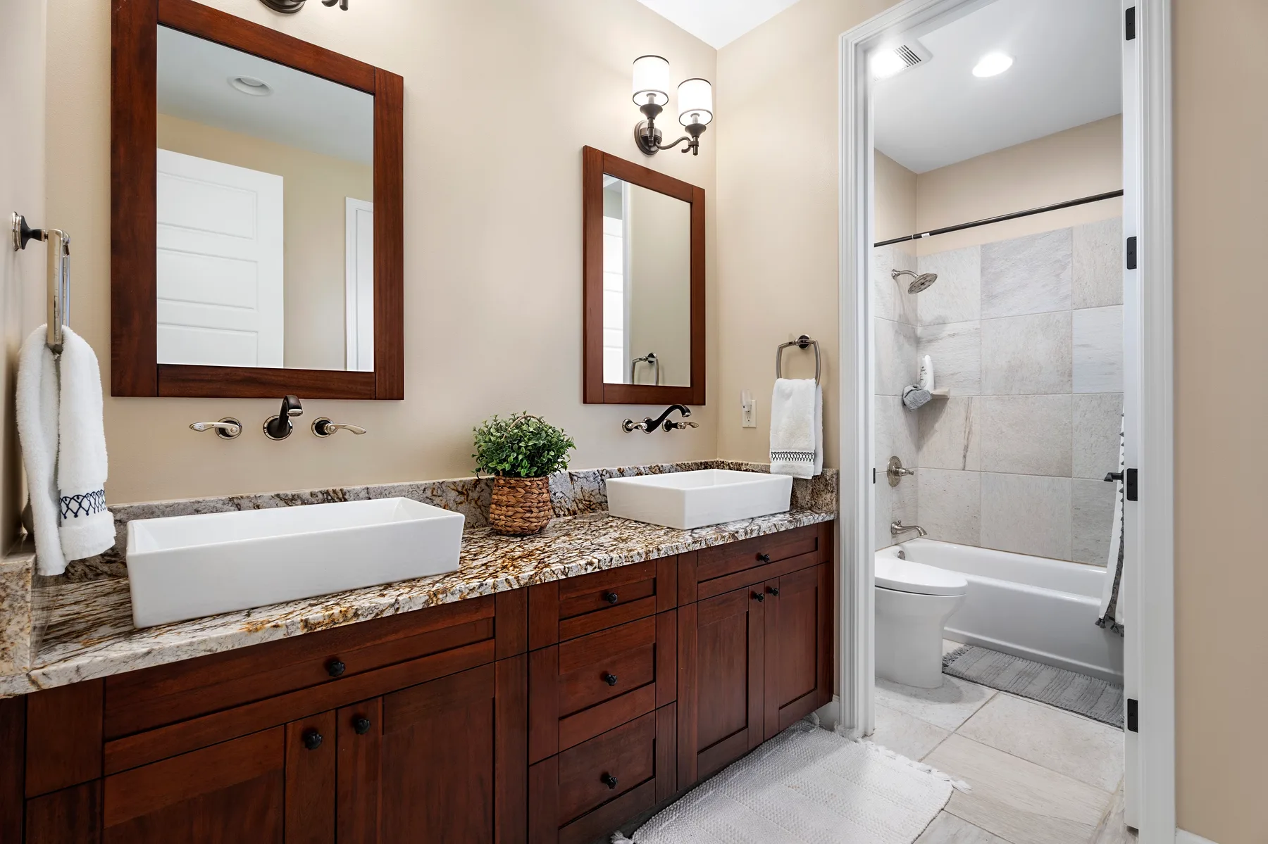 Un tocador de baño con dos lavabos da a una puerta abierta hacia una bañera y ducha con azulejos.