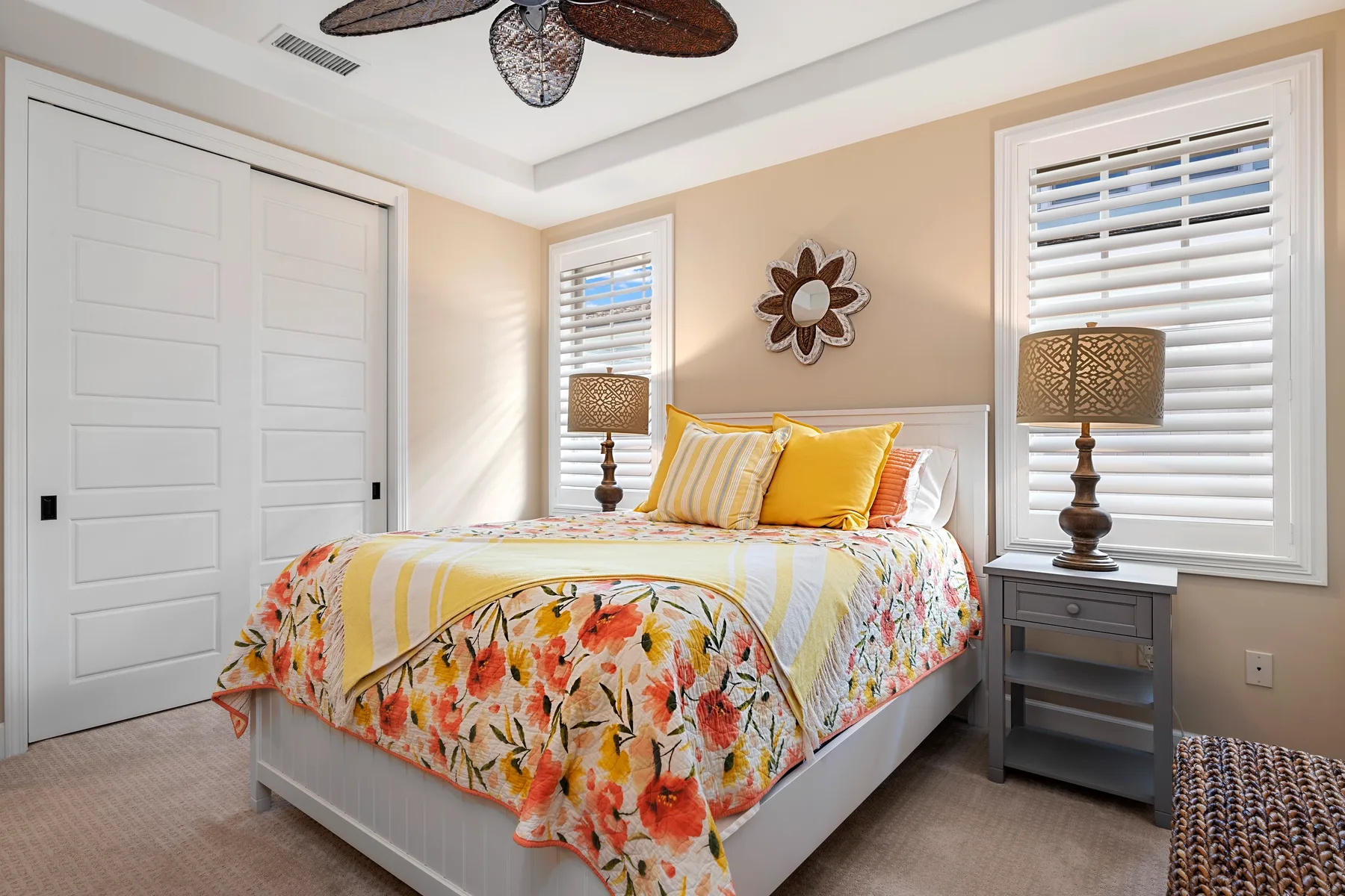 Un dormitorio luminoso con una cama vestida con ropa de cama floral colorida y ventanas con persianas.