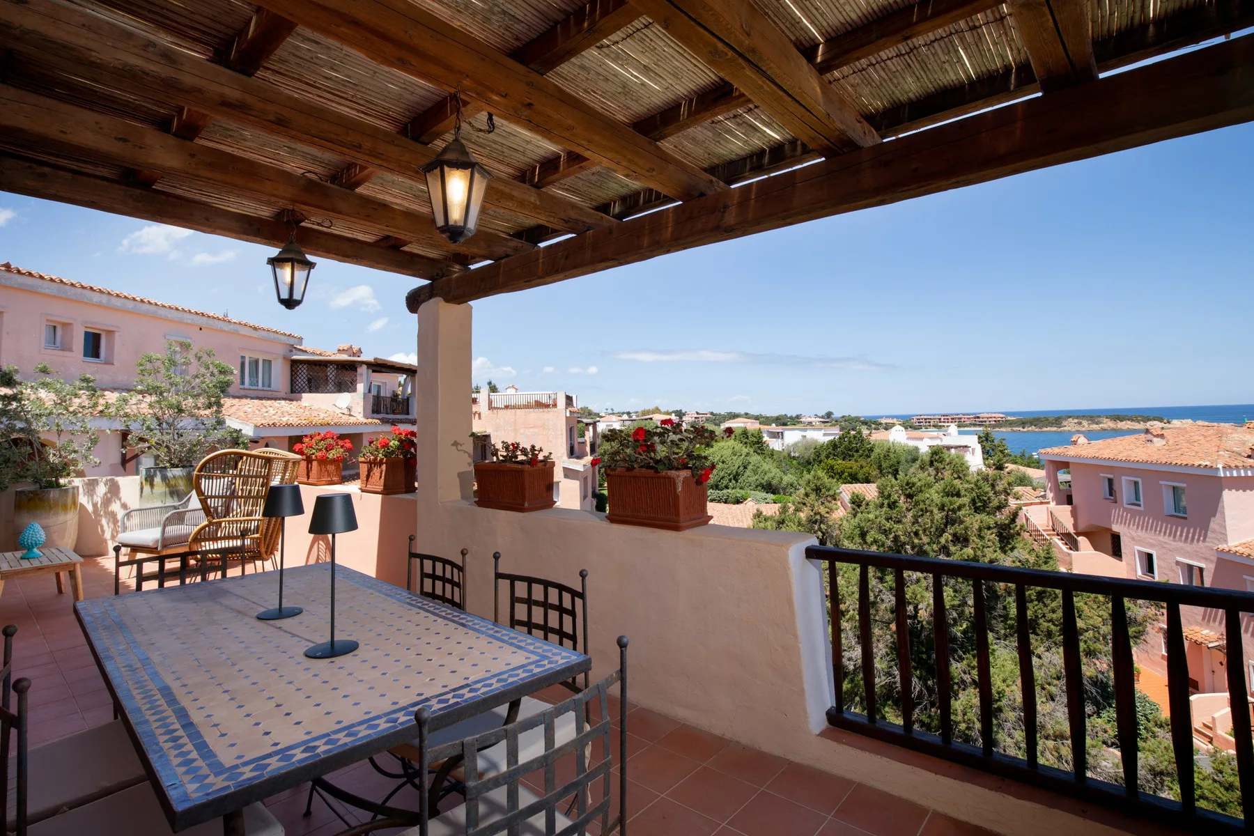 Una terraza cubierta con mesa de azulejos, asientos y vistas al mar.